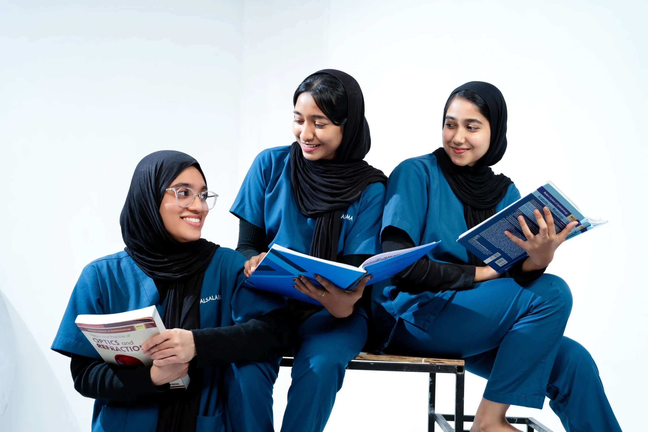 Three ophthalmology students in blue scrubs studying together with books and notes, reflecting collaborative learning and academic excellence